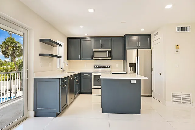 a large kitchen with stainless steel appliances kitchen island granite countertop a refrigerator and a sink
