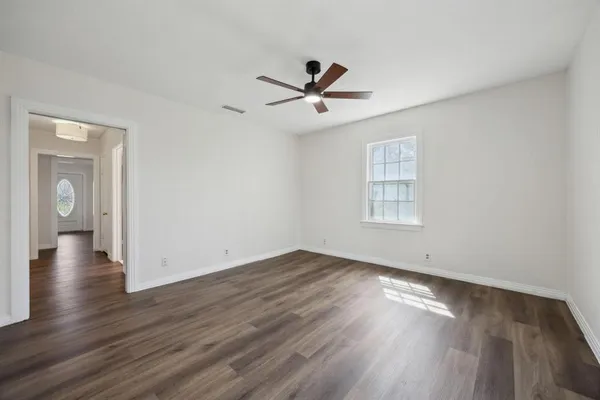 an empty room with wooden floor ceiling fan and windows