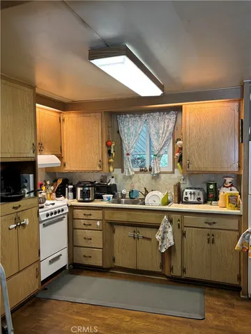 a kitchen with stainless steel appliances a white refrigerator a sink a stove and white cabinets with wooden floor