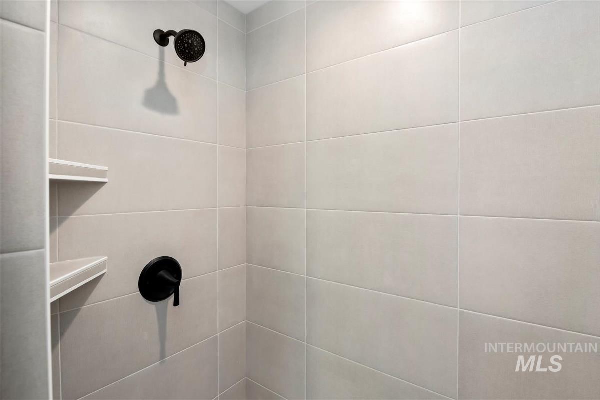752 South Calhoun Lane Star, ID 83669 - Photo 21 of 45 Shower enclosure featuring light-toned rectangular tilework, matte black shower head, matte black single-handle faucet, and built-in corner shelving