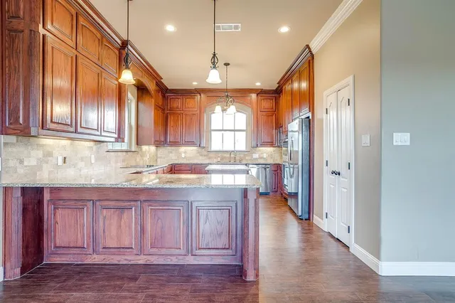 a kitchen with stainless steel appliances granite countertop a refrigerator a sink dishwasher a stove and white cabinets with wooden floor