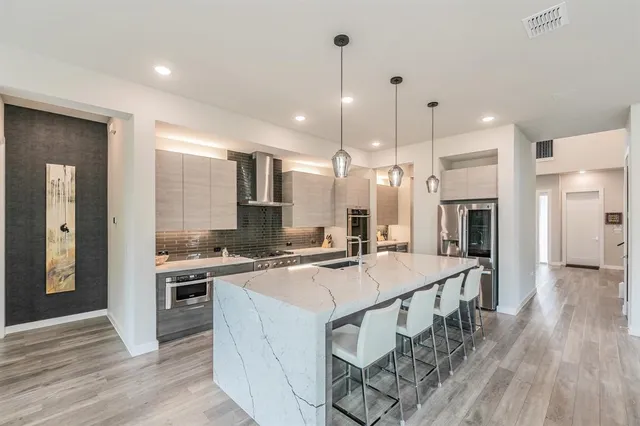 a open kitchen with stainless steel appliances granite countertop a stove top oven a refrigerator a sink and a dining table with wooden floor