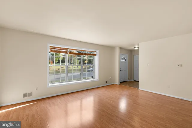 a view of an empty room with wooden floor and a window