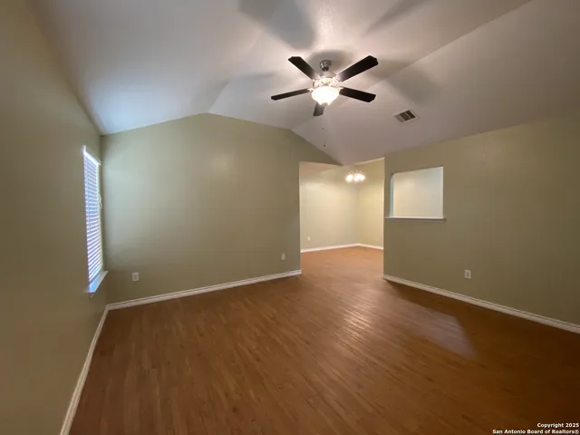 a view of an empty room with wooden floor and a fan
