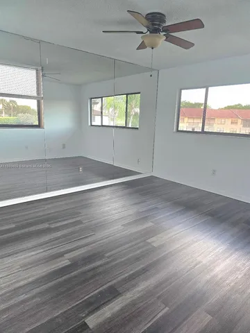 an empty room with wooden floor windows and ceiling fan