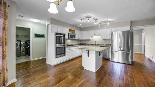 a kitchen with kitchen island granite countertop stainless steel appliances cabinets a wooden floor and a sink