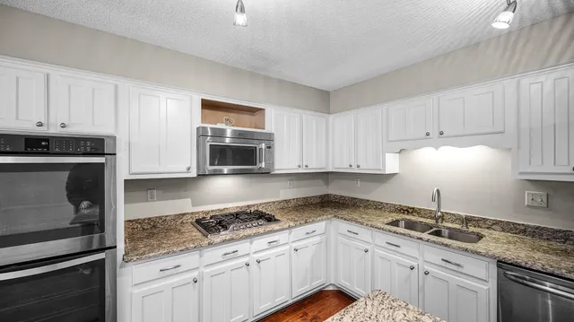 a kitchen with granite countertop a sink stainless steel appliances and white cabinets