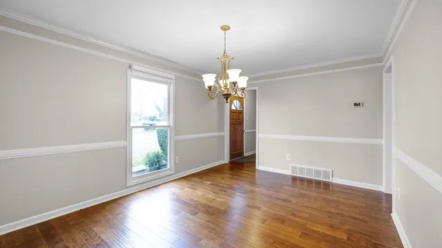 an empty room with wooden floor chandelier and windows