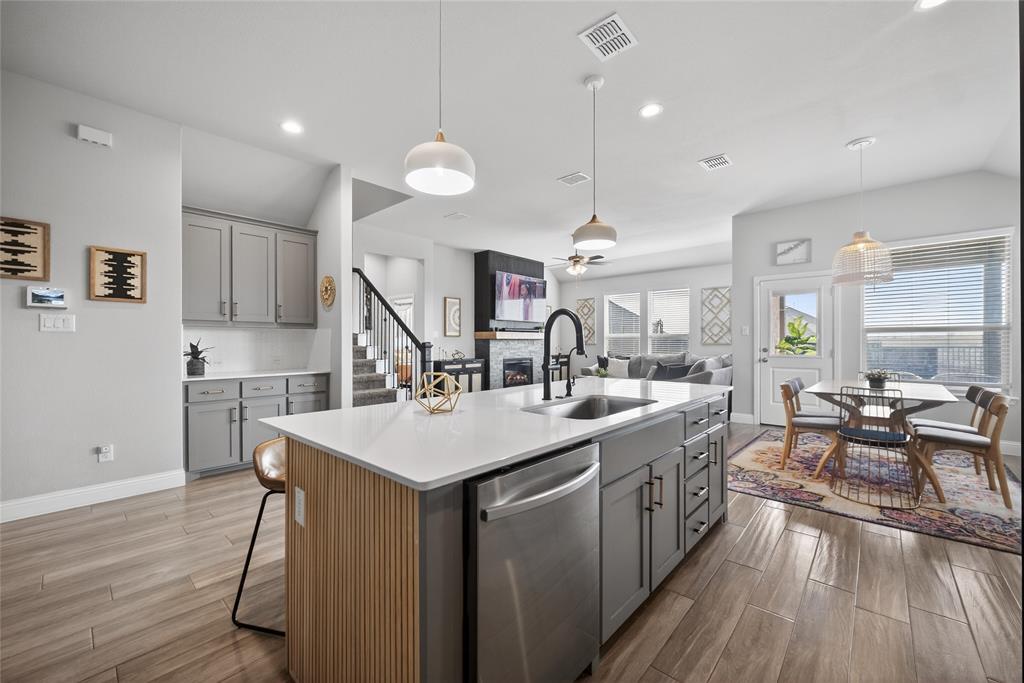 2252 Knightsgate Road Argyle, TX 76226 - Photo 10 of 36 Kitchen featuring gray cabinetry, a kitchen island with sink, a stone fireplace, stainless steel dishwasher, and lofted ceiling