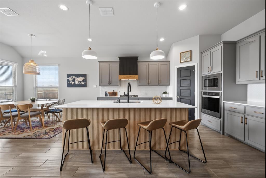 2252 Knightsgate Road Argyle, TX 76226 - Photo 8 of 36 Kitchen with gray cabinets, decorative light fixtures, a kitchen breakfast bar, stainless steel appliances, and a kitchen island with sink