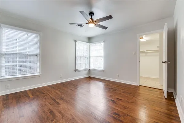 an empty room with wooden floor fan and windows