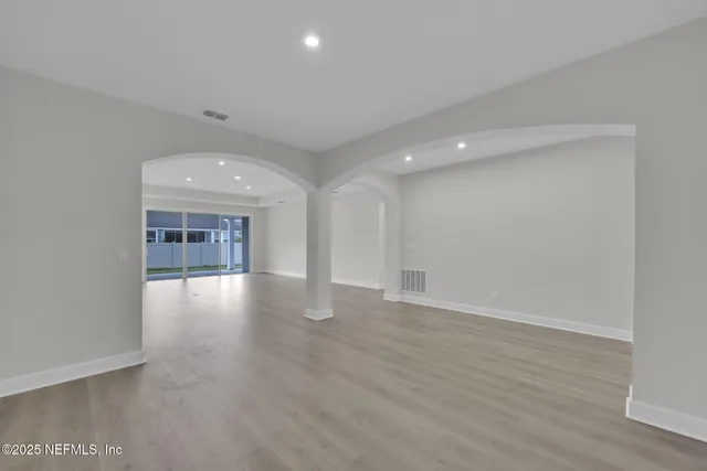 a view of an empty room with wooden floor and a kitchen