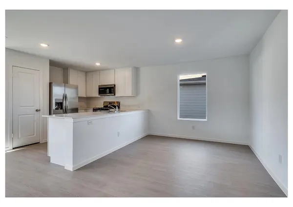 a kitchen with stainless steel appliances granite countertop a stove a sink a refrigerator white cabinets and a wooden floor