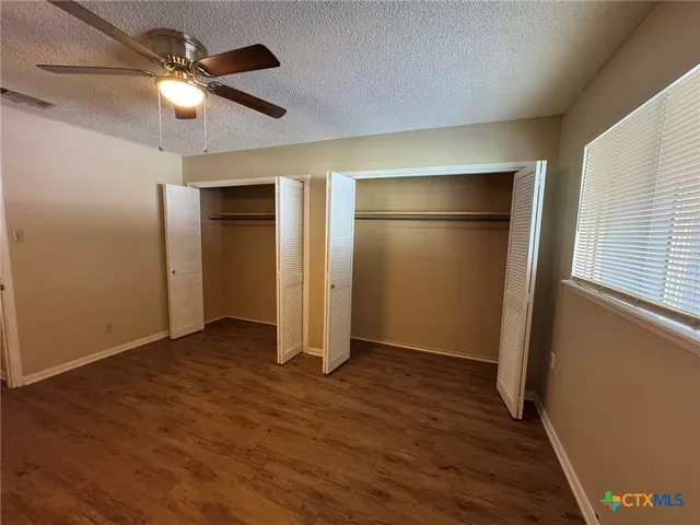 an empty room with wooden floor fan and windows