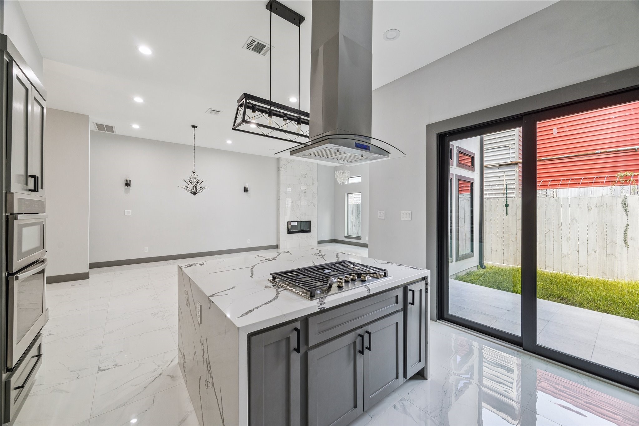 2323 Tuam Street Houston, TX 77004 - Photo 11 of 24 Sliding glass doors open to the patio, showcasing a kitchen anchored by a spacious island with built-in cooktop and a modern hood vent. Double ovens, sleek cabinetry, and clean finishes combine convenience with style.