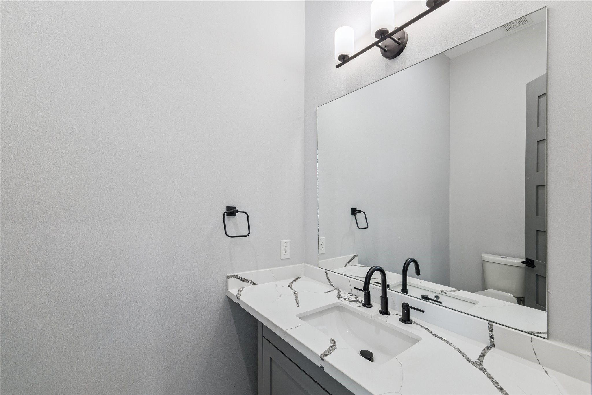 2323 Tuam Street Houston, TX 77004 - Photo 12 of 24 Quartz counters with striking veining and matte black fixtures bring a modern touch to the powder bath. A spacious mirror and wall-mounted lighting ensure a bright, inviting atmosphere that balances practicality with style.