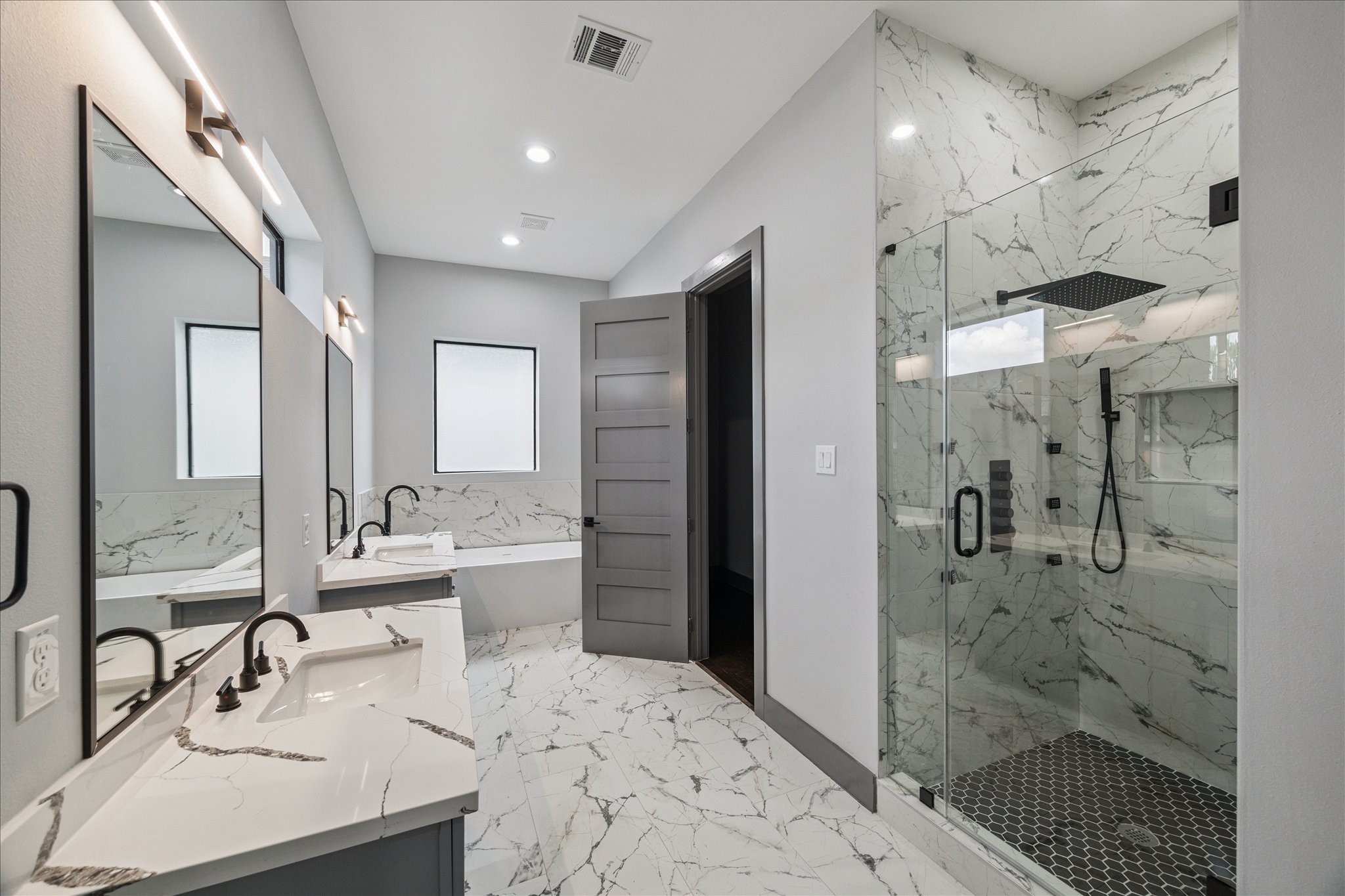 2323 Tuam Street Houston, TX 77004 - Photo 15 of 24 The primary bathroom is anchored by dual vanities, a glass-enclosed shower, and a soaking tub set beneath a window. Coordinated tilework ties the space together, accented by dark fixtures for contrast.