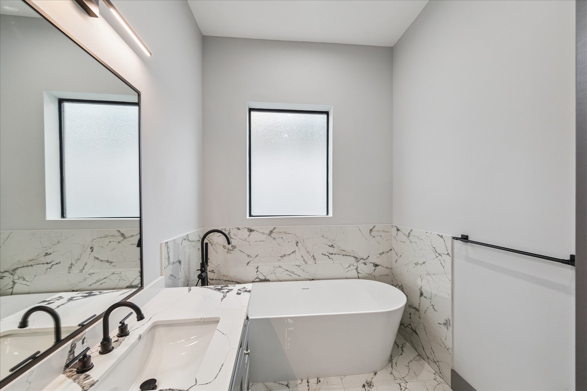 2323 Tuam Street Houston, TX 77004 - Photo 16 of 24 Deep soaking tub that serves as the centerpiece of this bathroom. Dual sinks with dark fixtures balance style and utility, while frosted windows bring in soft, natural light with privacy.