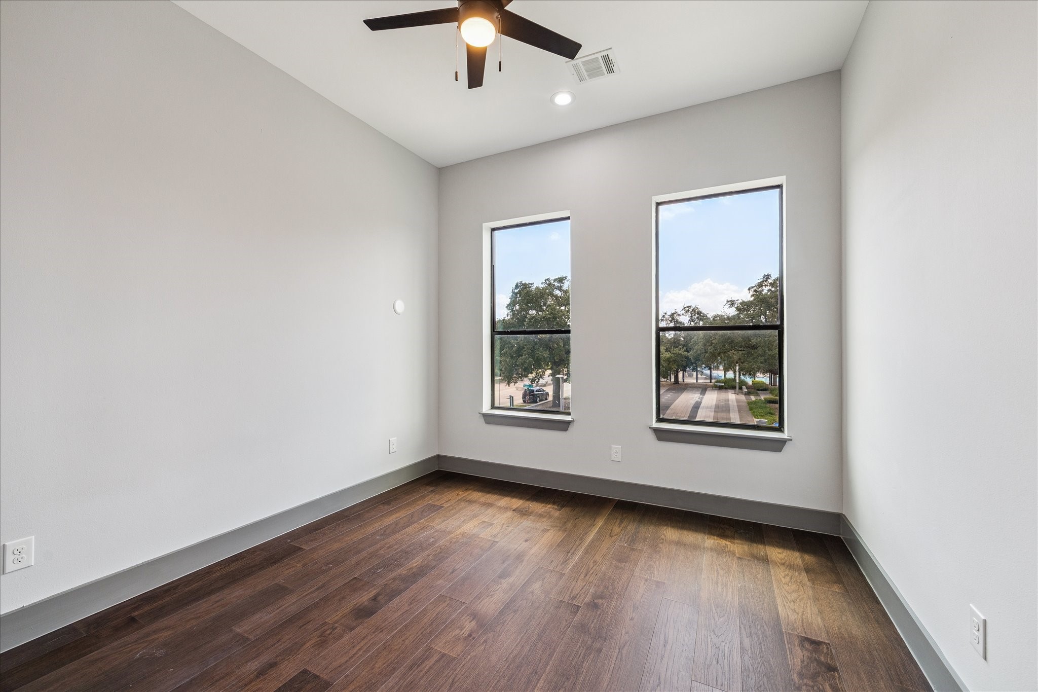 2323 Tuam Street Houston, TX 77004 - Photo 18 of 24 Large windows highlight the warm wood floors and neutral palette of this secondary bedroom. A ceiling fan adds comfort, making the space versatile for relaxation, guests, or a home office.