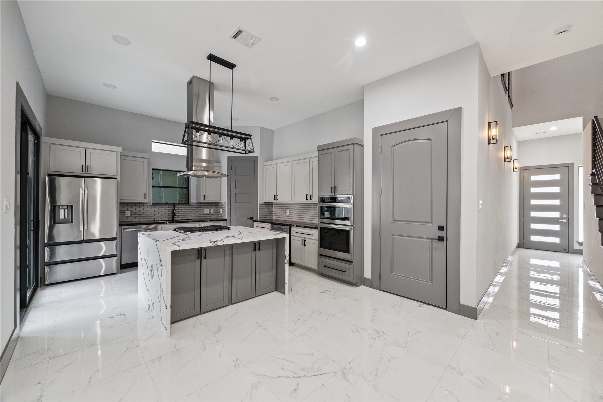 2323 Tuam Street Houston, TX 77004 - Photo 8 of 24 The kitchen showcases a striking island clad in marble-style surfaces, creating a strong focal point for the space. Soft gray cabinetry is paired with a polished tile backsplash, delivering a refined and timeless look.