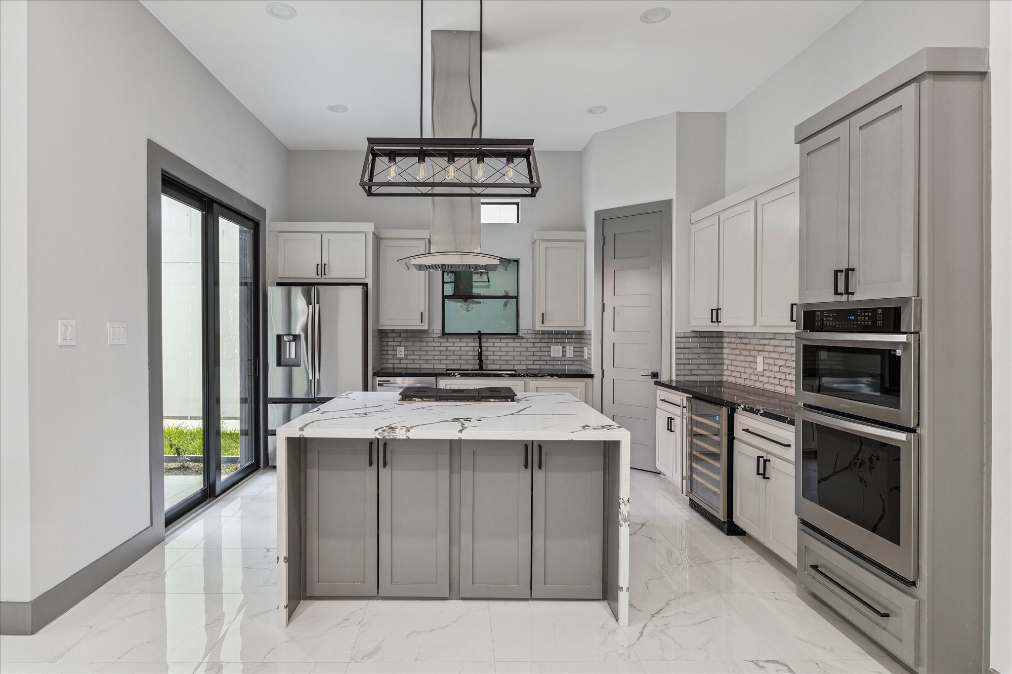 2323 Tuam Street Houston, TX 77004 - Photo 9 of 24 A light-filled kitchen with clean lines showcases a waterfall island, stainless appliances, and double ovens for everyday ease. The vent hood and brick-pattern backsplash create a striking focal point, complemented by under-cabinet lighting and a beverage cooler for added functionality.
