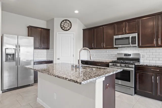 a kitchen with granite countertop a stove top oven microwave and refrigerator