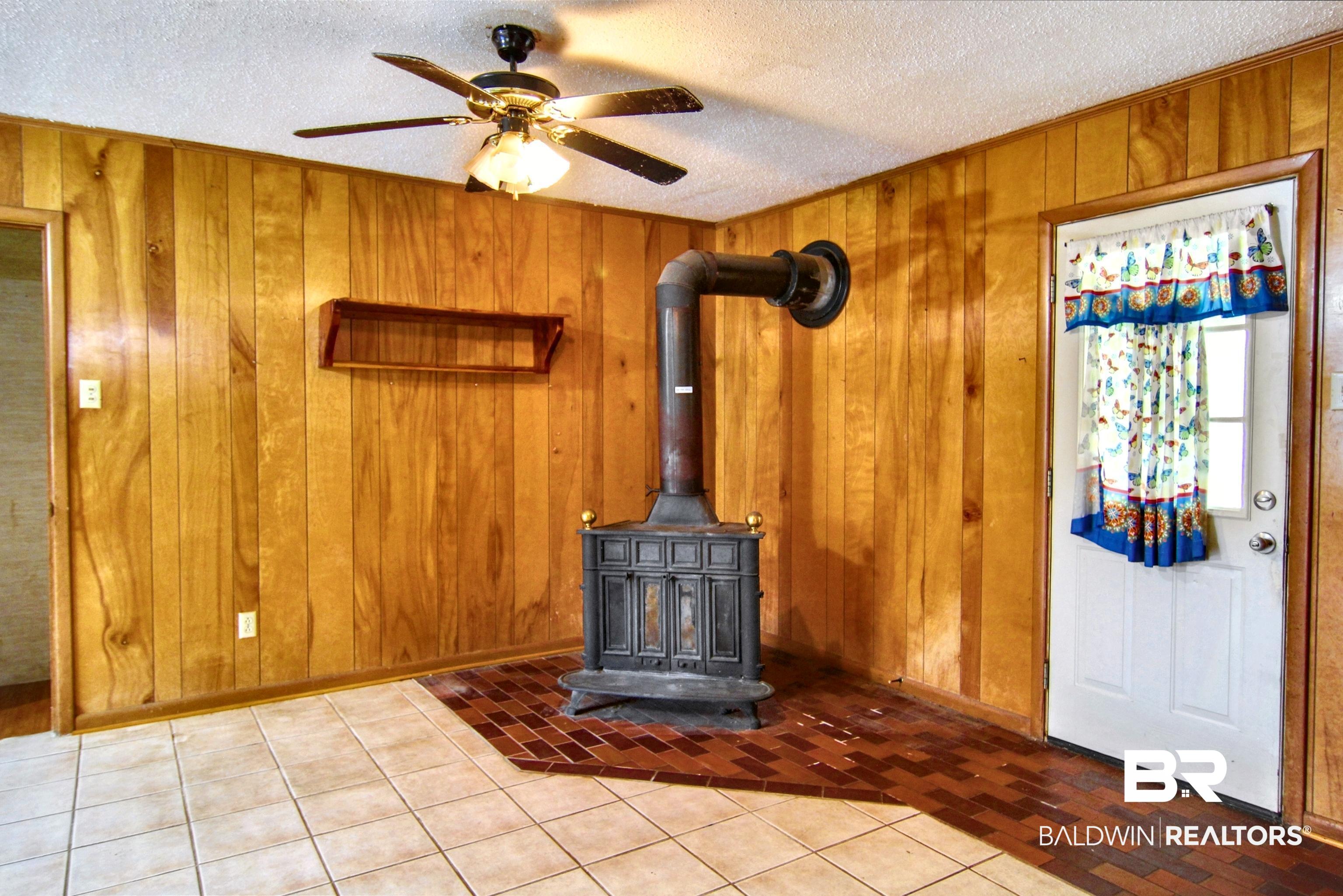 12897 County Road 65 Foley, AL 36535 - Photo 12 of 21 Details with wooden walls, a wood stove, a textured ceiling, baseboards, and ceiling fan