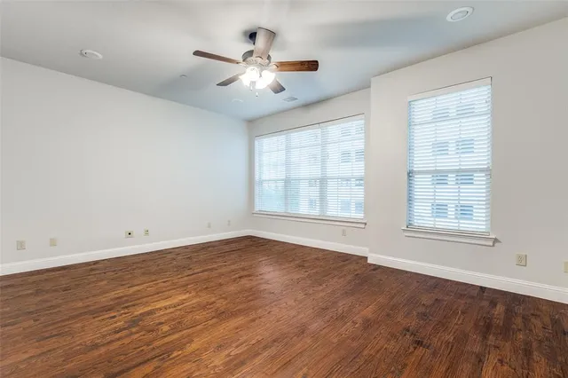 an empty room with wooden floor chandelier fan and windows