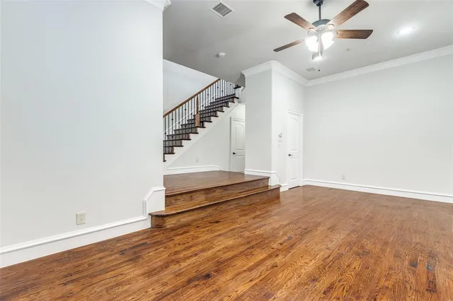 a view of an empty room with wooden floor and a ceiling fan