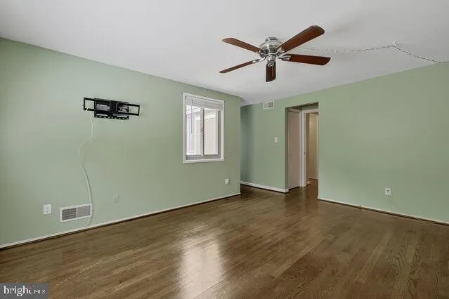 a view of an empty room with wooden floor and a ceiling fan