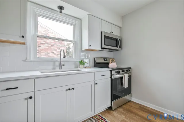 a kitchen with stainless steel appliances granite countertop white cabinets a sink a stove a microwave and view living room