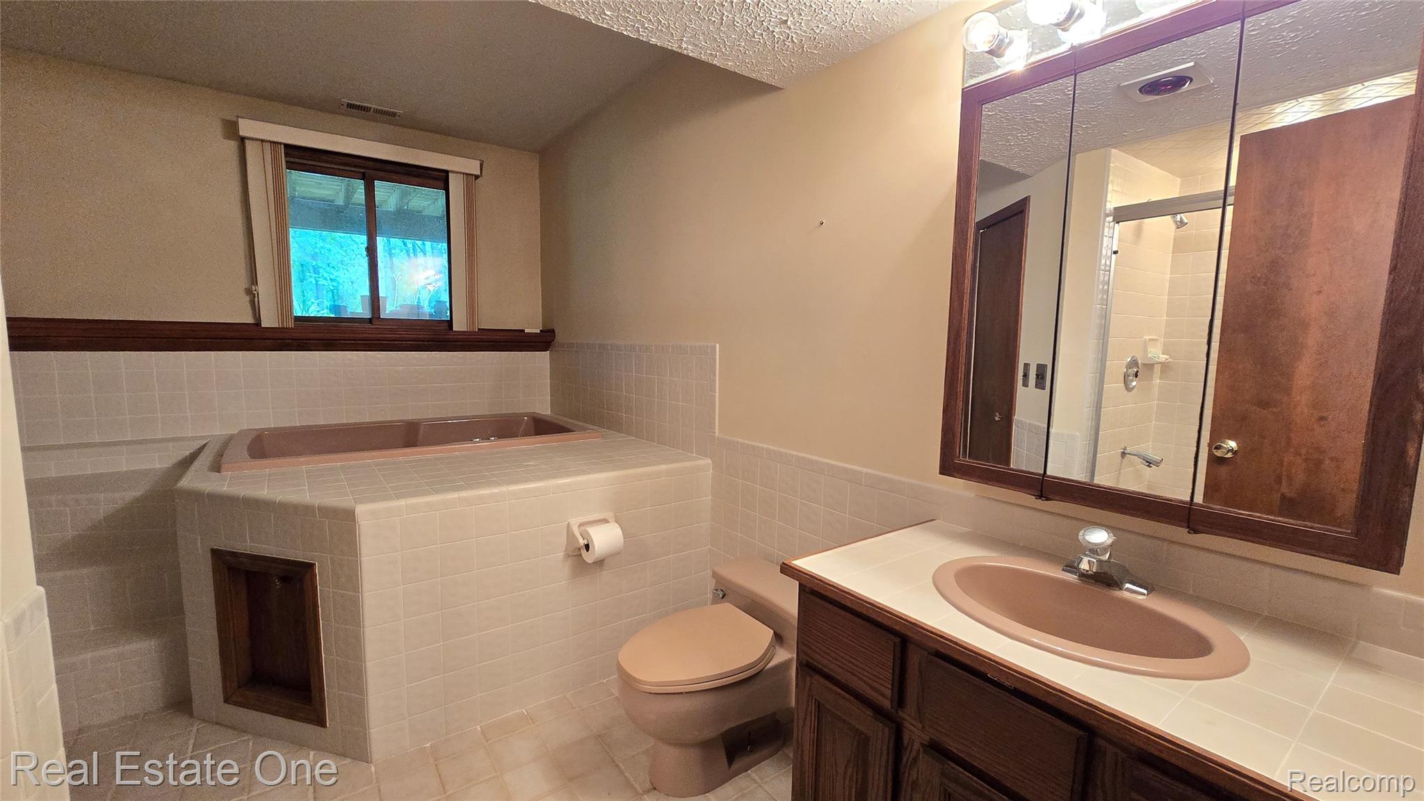 8950 Wise Road Commerce Township, MI 48382 - Photo 31 of 39 Bathroom featuring a tiled built-in tub, a wood-finish vanity with a drop-in sink, and a mirrored medicine cabinet