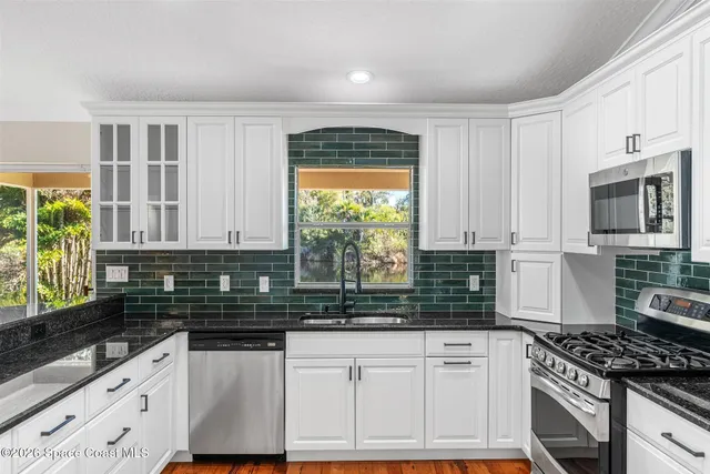 a kitchen with stainless steel appliances a stove a sink a refrigerator cabinets and a window
