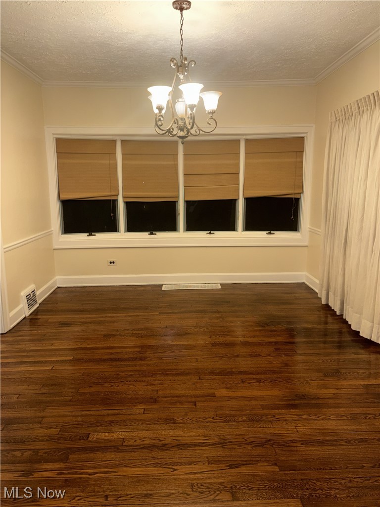 1019 Quilliams Road Cleveland Heights, OH 44121 - Photo 9 of 32 Empty room featuring a textured ceiling, dark wood-type flooring, hanging lights, and ornamental molding