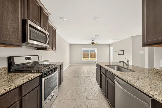 a kitchen with granite countertop stainless steel appliances a sink stove top oven and cabinets