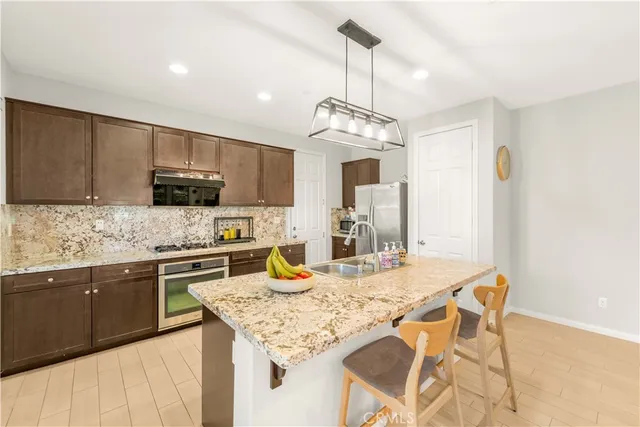 a kitchen with stainless steel appliances granite countertop a sink a stove a refrigerator cabinets and a dining table