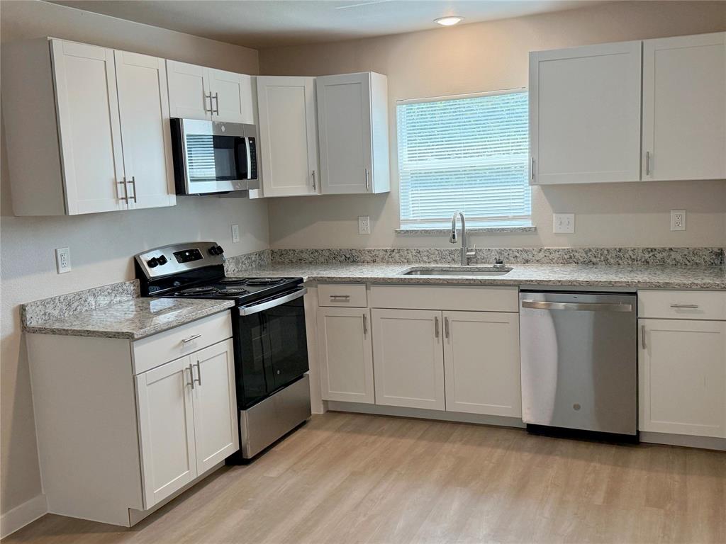 a kitchen with stainless steel appliances granite countertop white cabinets a sink a stove a microwave and dishwasher with wooden floor