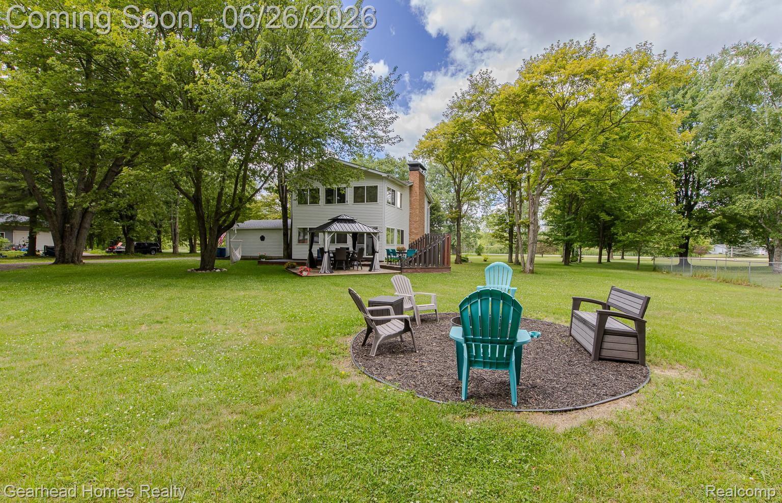 Expansive green lawn with mature shade trees, a dedicated fire pit area with seating, and a paved patio featuring a gazebo