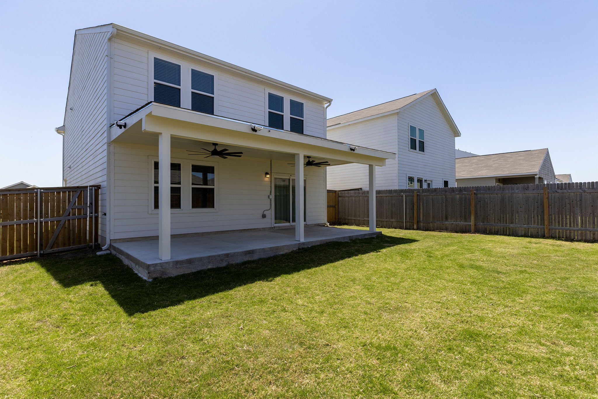 409 Line Of Fire Way Jarrell, TX 76537 - Photo 29 of 30 Expansive backyard featuring a manicured lawn, full wood privacy fence, covered patio with ceiling fans, exterior lighting, and open green space.