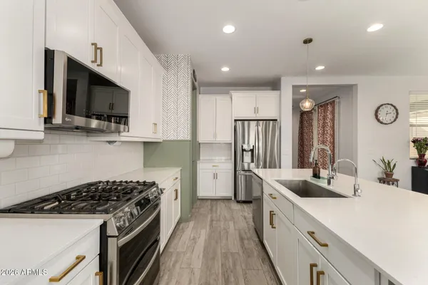 a kitchen with stainless steel appliances a sink dishwasher a stove top oven a refrigerator with grey cabinets and wooden floor