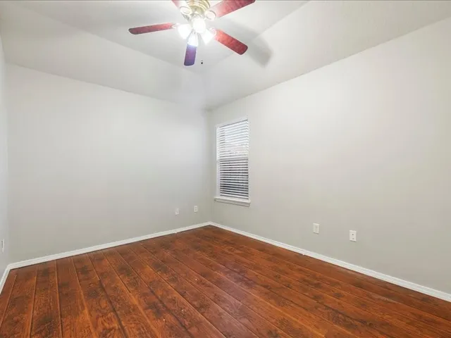 an empty room with wooden floor chandelier fan and windows