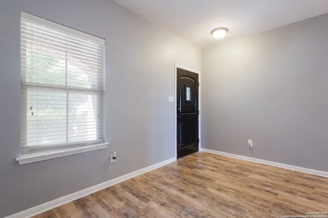 a view of an empty room with wooden floor and a window