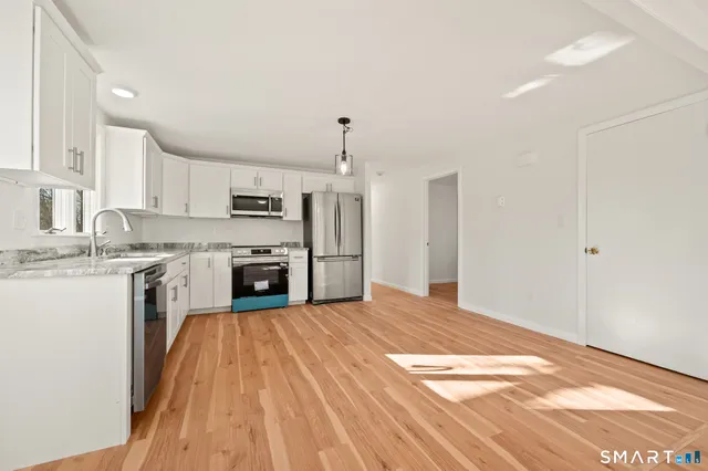 a large kitchen with granite countertop a stove a sink dishwasher and a refrigerator with wooden floor