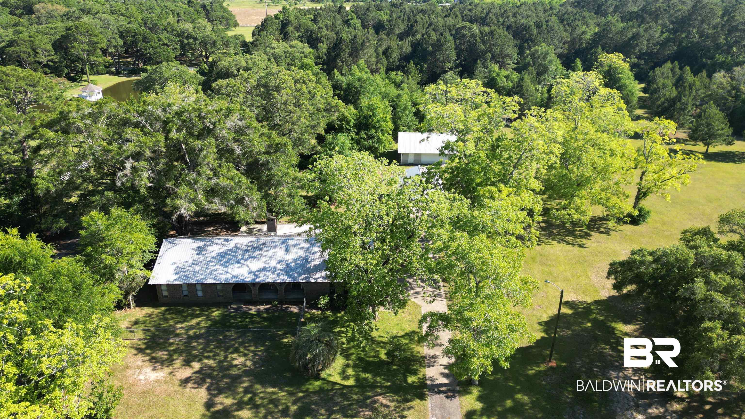 33370 Highway 98 Lillian, AL 36549 - Photo 43 of 58 Property set amidst mature trees with a visible pond, featuring a main structure with a light-colored roof and an additional structure