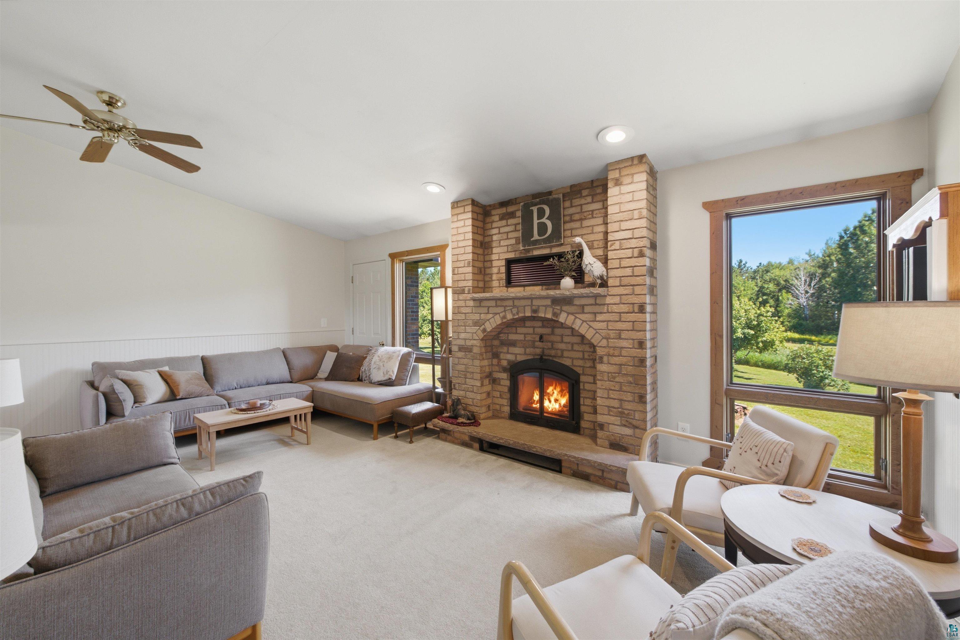 64260 Jolma Road Ashland, WI 54806 - Photo 13 of 35 Brick fireplace with integrated wood stove, large window with wood trim, ceiling fan, carpeted flooring, and recessed lighting