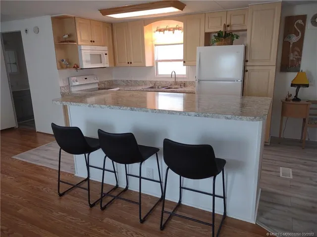 a kitchen with stainless steel appliances granite countertop a refrigerator a stove a sink and chairs with wooden floor