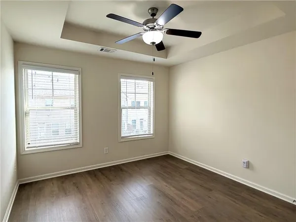an empty room with wooden floor ceiling fan and windows