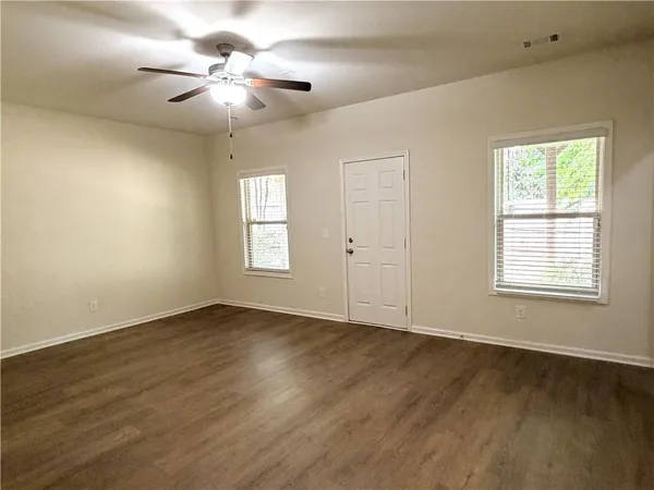 an empty room with wooden floor chandelier fan and windows