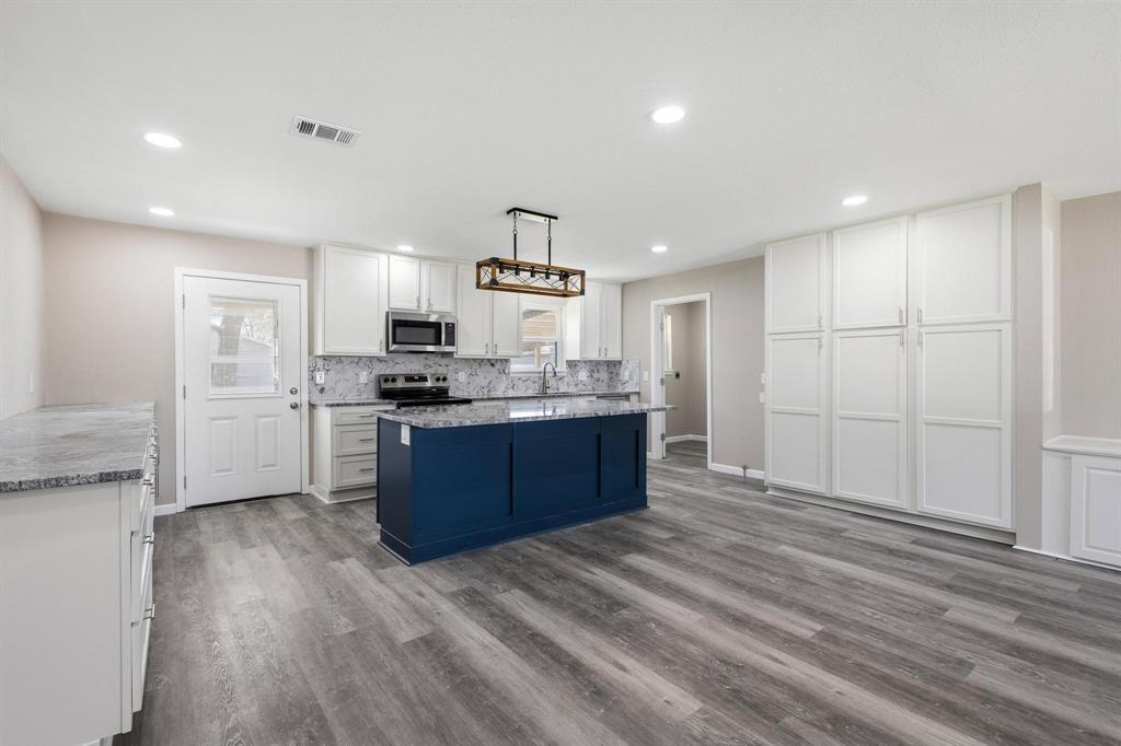 1704 Harris Street Gainesville, TX 76240 - Photo 7 of 21 Kitchen with a center island, stainless steel appliances, two tone cabinetry, dark wood-type flooring, and light stone counters
