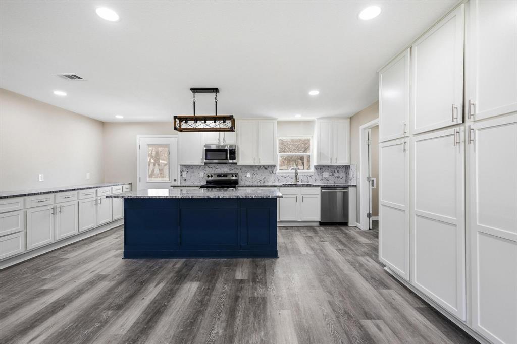 1704 Harris Street Gainesville, TX 76240 - Photo 8 of 21 Dual tone kitchen featuring a kitchen island, stainless steel appliances, tasteful backsplash, dark wood-type flooring, and dual tone cabinets